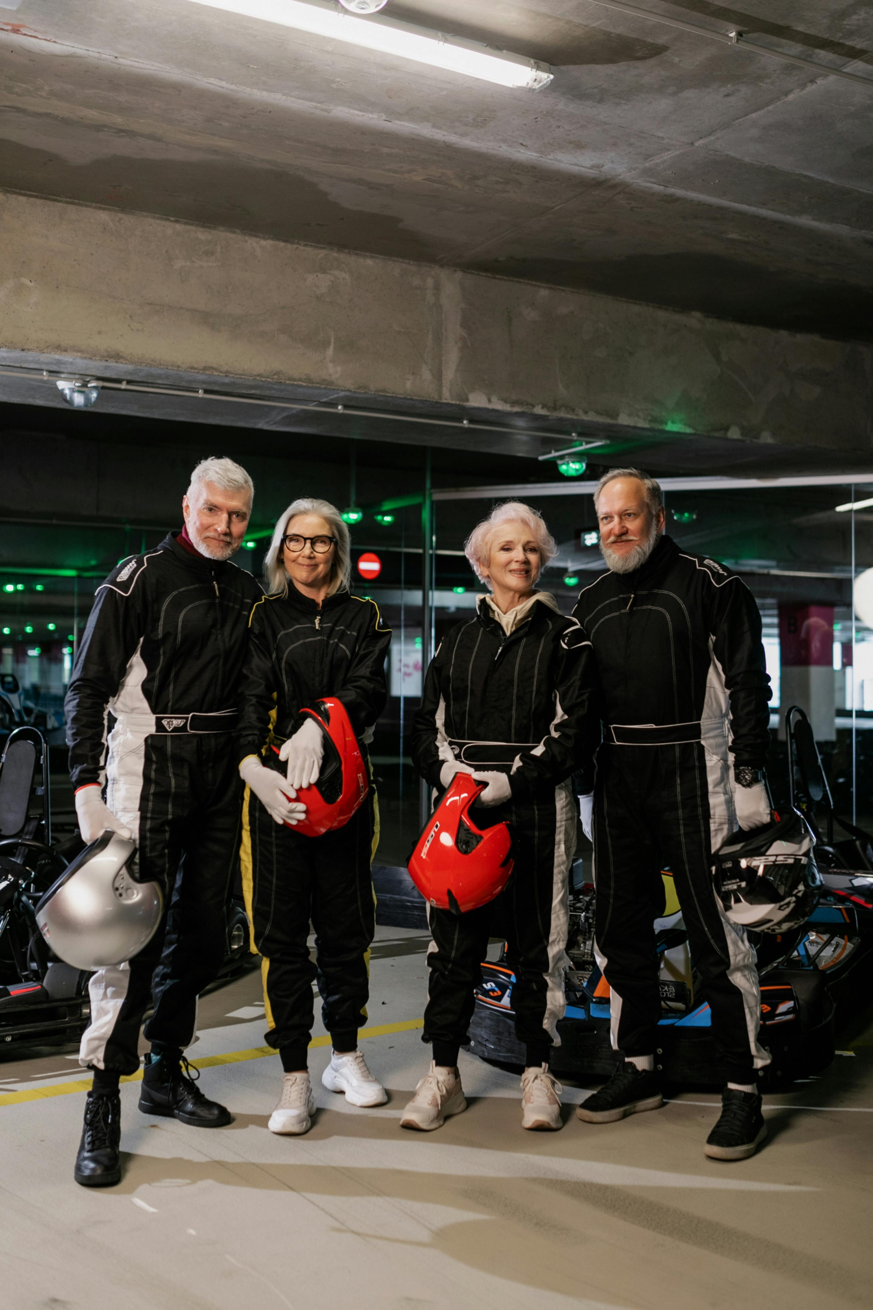 A group of senior adults in racing suits posing at an indoor karting track.
